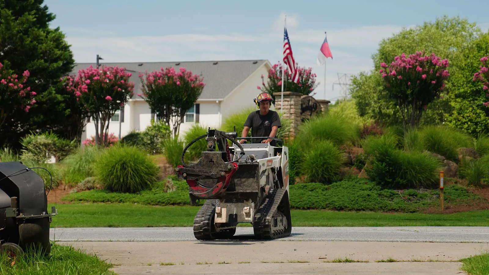 Stump grinder at work on a front lawn, operator in hard hat and ear defenders